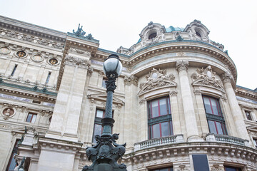 Exterior of the Palais Garnier, the historic Paris opera house, in the Beaux-Arts style. A lamppost stands prominently in front of its detailed facade