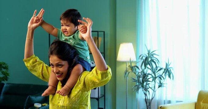 Indian infant boy crying while sitting on mother&rsquo;s shoulder in cozy modern living room, showing signs of irritation or discomfort, expressing emotion and needing comfort, love, and gentle care