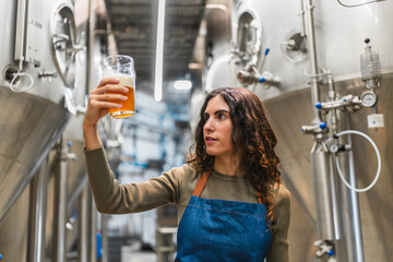 Female brewer holding a glass of beer, examining clarity and color during quality control in a modern craft beer facility
