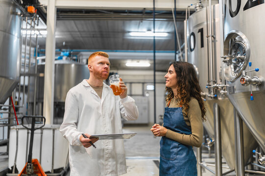 Man and woman working at a brewery, conducting quality control, tasting beer, and inspecting production process