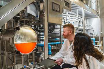 Production engineers collaborating, monitoring brewing process and quality control in a modern stainless steel craft beer factory