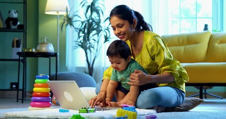 Indian young mother working from home on laptop with infant baby boy sitting on lap, balancing work and motherhood with love, care, affection, and modern family life indoors - Powered by Adobe