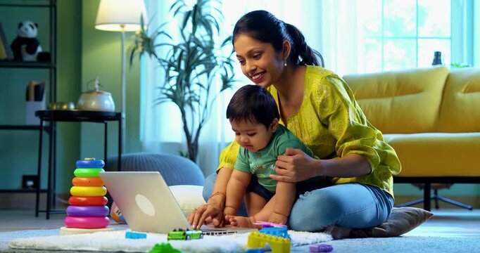 Indian young mother working from home on laptop with infant baby boy sitting on lap, balancing work and motherhood with love, care, affection, and modern family life indoors