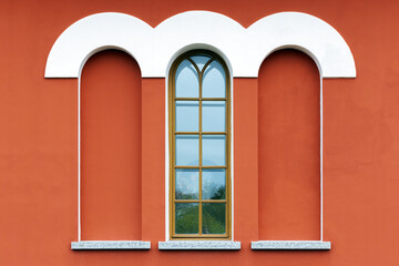 Red building facade features a white rounded arches and a tall window and niches