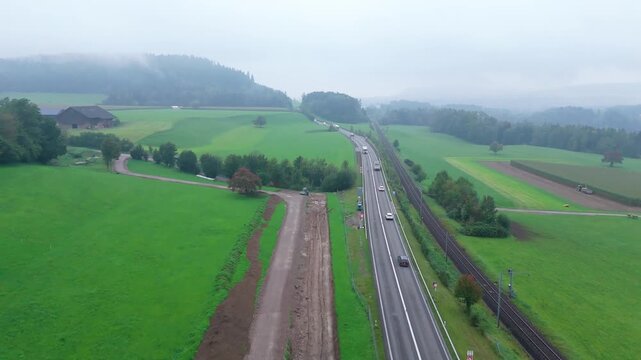 Morning traffic flows beside a rural railway through green fields, Aerial