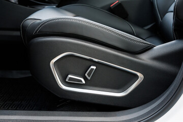 Side view of black leather car seat with white stitching and electric adjustment controls in metallic trim