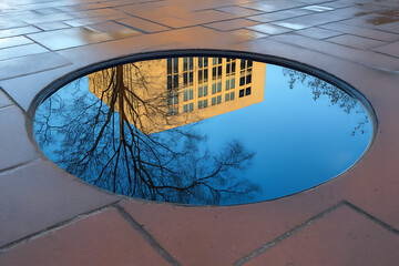 Circular Puddle Reflecting Sky and Building &ndash; Urban Nature Symmetry.