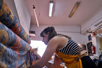 Obraz premium Female upholsterer working in workshop, applying colorful patterned fabric to furniture, using a staple gun for restoration