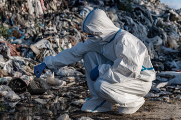 An environmental worker in protective gear collects samples at a landfill site, highlighting ongoing pollution and waste management issues