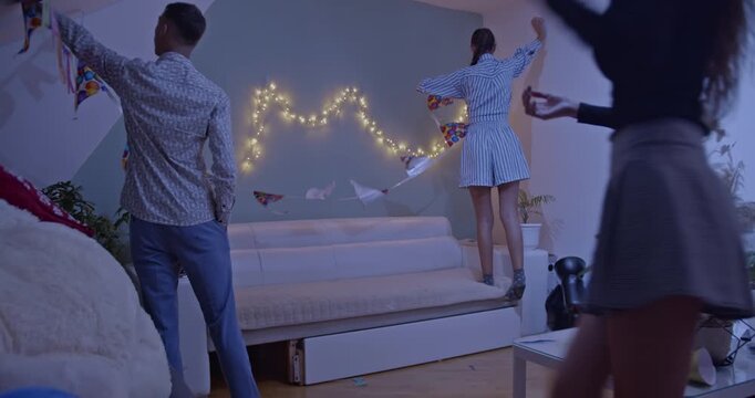 Friends eagerly decorating a home for a lively birthday party celebration, hanging festive banners and string lights. They are preparing the living room for a fun gathering.