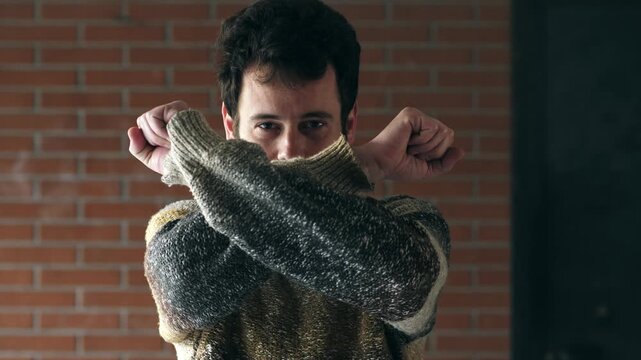 A young man with dark hair in a sweater crosses his arms in front of his body, expressing refusal, disagreement, or that no one can pass, showing assertiveness and boundary setting indoors.