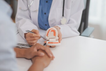 Dentist consultation - patient visit at the dental clinic office. Female dentist wearing dentures to explain teeth Recommend guidelines for orthodontics Dentist giving advice on patient's condition