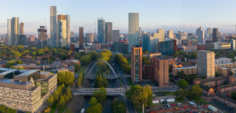 Aerial sunrise view above Princess Road featuring Manchester&rsquo;s skyline framed by trees and modern architecture.