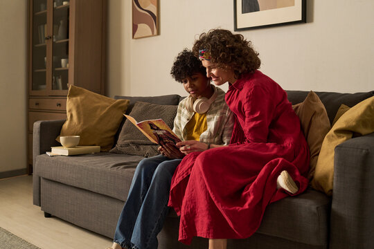 Mother and son reading a comic book together on the living room sofa