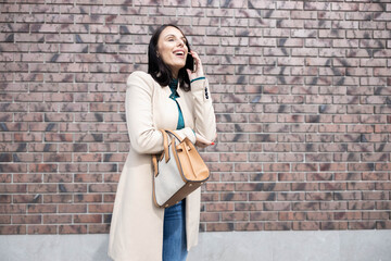 This image features an elegant woman joyfully conversing on her phone, showcasing her fashionable attire and cheerful demeanor.