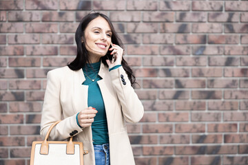 This photo showcases a smiling woman speaking on her phone, radiating positivity and style against a urban brick wall.