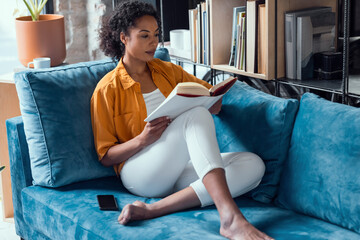 Woman relaxing on blue couch reading a book at home
