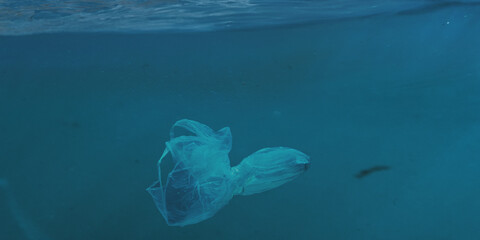 Plastic bag floating underwater in deep blue ocean. Concept of marine pollution, environmental...