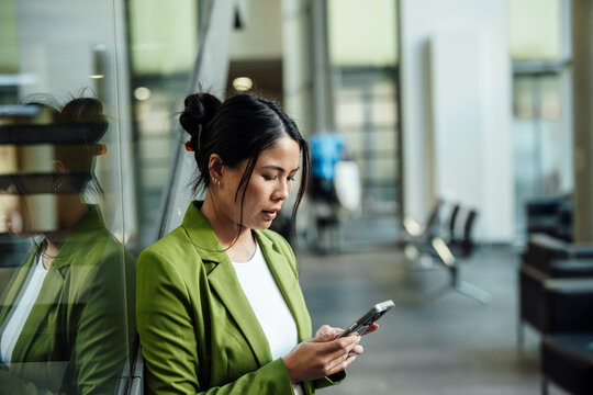 Businesswoman in green jacket using smartphone indoors