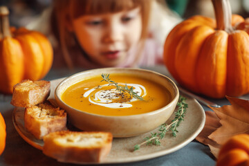 Cozy Autumn Pumpkin Soup with Garlic Bread and Child Looking with Anticipation – Warm Family and Halloween Food Concept	
