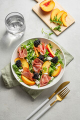 Fresh salad with peaches, arugula, feta, prosciutto and berries in a plate on a light background
