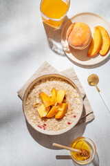 Oatmeal with peaches and nuts  in a bowl on a light background with honey