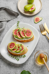 Sweet toasts with fresh figs, cheese, thyme, and honey on a gray background.