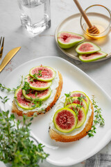 Sweet toasts with fresh figs, cream cheese, thyme, and honey on a marble background close up.