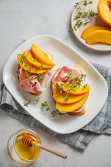 Toast with peach, cream cheese, ham and honey on a plate on a light background