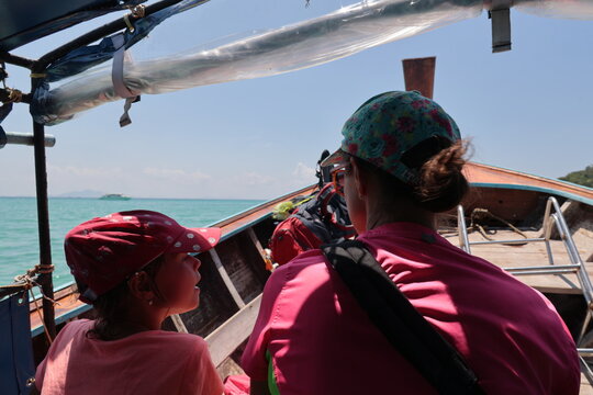 Mother and daughter in colorful clothes and hats riding a traditional Thai dhow boat near Phi Phi Island on a sunny day with blue sea background