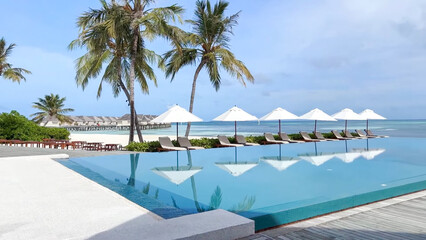 Infinity pool overlooking the stunning turquoise ocean, palm trees, and overwater villas under a bright blue sky at a luxury resort