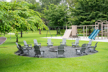 a group of gray Adirondack chairs circled around on a bonfire pit outside on a well maintained lawn 