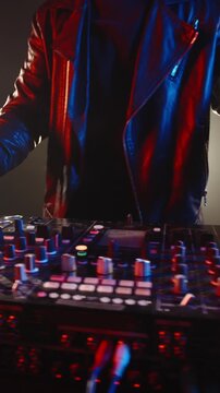 Slow motion vertical video of confident DJ mixing music on stage, beard man in leather jacket moving with rhythm in glowing lights, symbol of drive success and creative flow