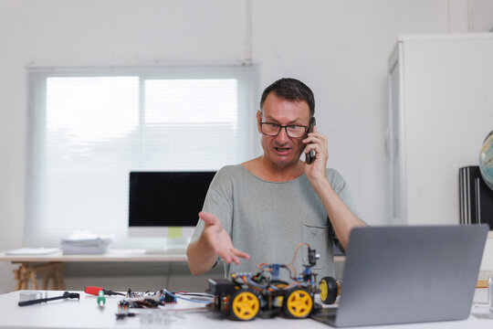 Man having stressed phone call while building robot car
