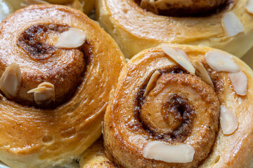 Freshly Baked Cinnamon Rolls with Almonds. A delicious close-up of warm, golden brown sweet buns right from the oven. Topped with sliced almonds, this homemade pastry is a perfect comfort food treat.