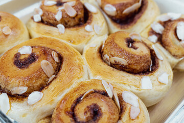 Freshly Baked Cinnamon Rolls with Almonds. A delicious close-up of warm, golden brown sweet buns right from the oven. Topped with sliced almonds, this homemade pastry is a perfect comfort food treat.