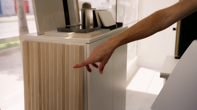 Male designer's hand choosing stone, ceramic, and wood veneer samples for new project, touching different textures and surfaces in modern showroom for home renovation and decoration