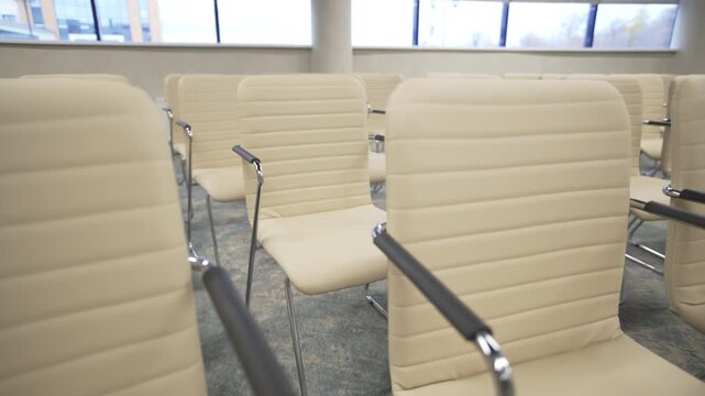 Rows of leather chairs with metallic armrests align near panoramic window. Glossy metallic details contrast soft white leather surfaces