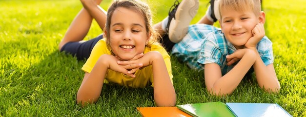 Happy child sitting on the field holding tablet. Boy sitting on the grass on sunny day. Home schooling or playing a tablet