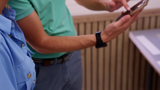 Close-up shot of male police officer using smartphone to demonstrate information to someone else, pointing at screen with his finger. Emphasizing integration of technology in policing