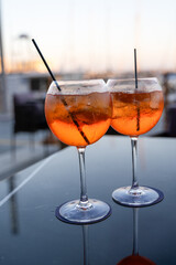 There are two glasses containing orange liquid with straws placed on a table