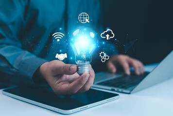 Businessman holding glowing blue light bulb with digital technology icons representing innovation, cloud computing, networking, and creative ideas for smart business and digital transformation.