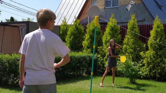 Youthful spirits and adult enjoy lively tethered ball game in vibrant, sunlit summer backyard, full of fun and recreation.
