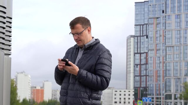 Urban man, initially engrossed in his smartphone, transitions from serious call to dismayed reaction while interacting with his screen against modern city backdrop.