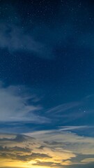 Fototapeta premium A night sky photograph featuring a gradient from a golden horizon, through clouds, to a deep blue with shimmering stars