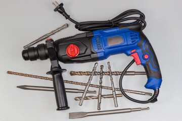 Electric rotary hammer and different drill bits on gray background