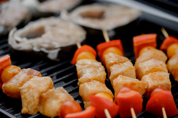 Fish skewers with tomatoes and steaks on a black barbecue grill