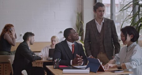 Diverse colleagues brainstorm and analyze data in a co working space. They discuss, strategize, and collaborate on a project using a tablet and documents. - Powered by Adobe