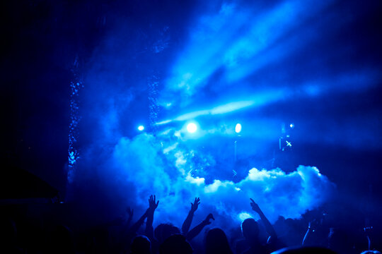 Crowd with hands up under blue lights and smoke at festival party