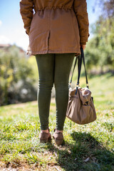 Stylish woman's casual fashion ensemble for outdoor adventures, featuring olive green leggings, a tan jacket, and a chic handbag in a natural setting.